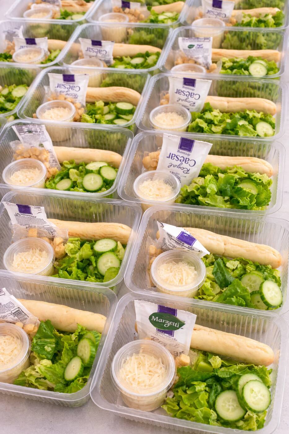 A grid of caesar salad trays with romaine, parmesan cups and breadsticks ready for service