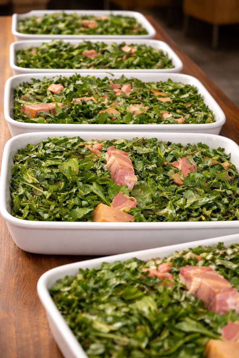 Long pans of slow-braised collard greens with smoked ham, plated for the cafeteria line